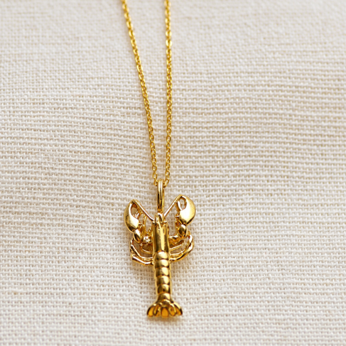 Gold lobster pendant necklace with a detailed lobster charm on a delicate silver-colored chain, worn around the neck.