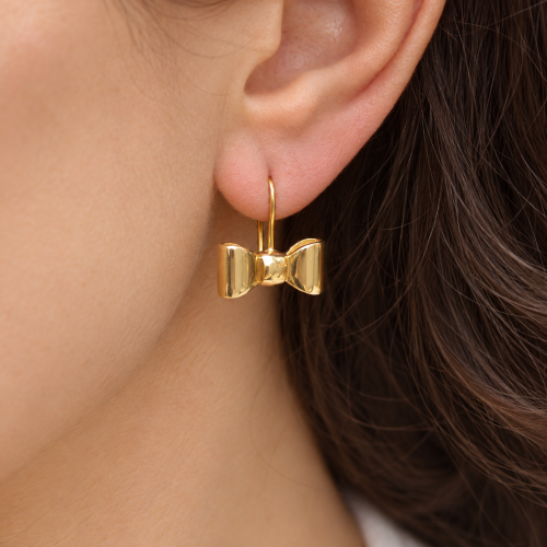 Close-up of a gold bow-shaped drop earring worn on the ear