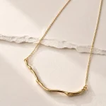 Gold organic bar necklace with a sculptural wavy pendant on a delicate chain